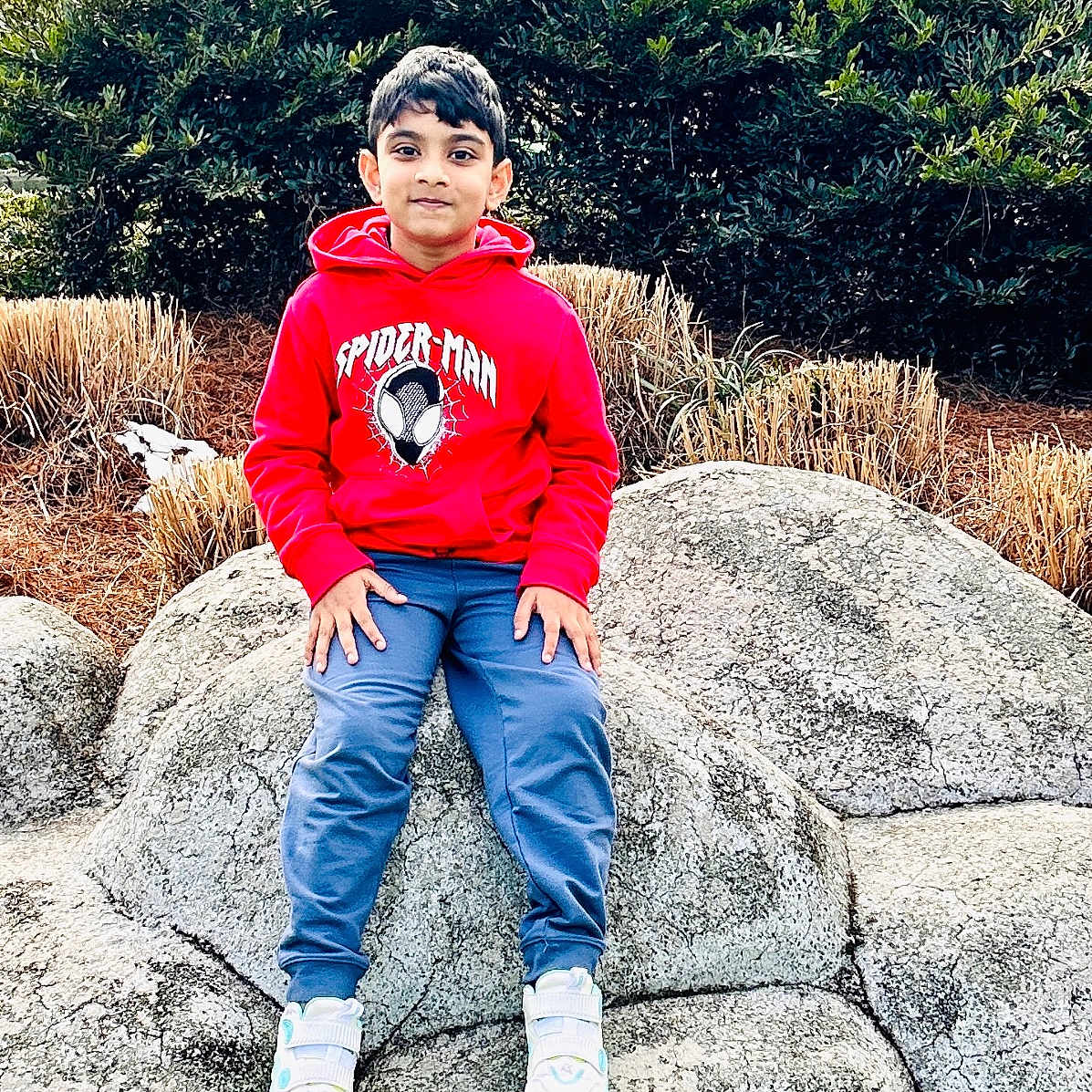 Aayan joined the competition — help win amazing prizes! blue_pants, boy, bushes, casual_clothing, child, daylight, greenery, model_house, nature, outdoor, park, portrait, red_hoodie, relaxed, rock, sitting, smiling, sneakers, spiderman, young