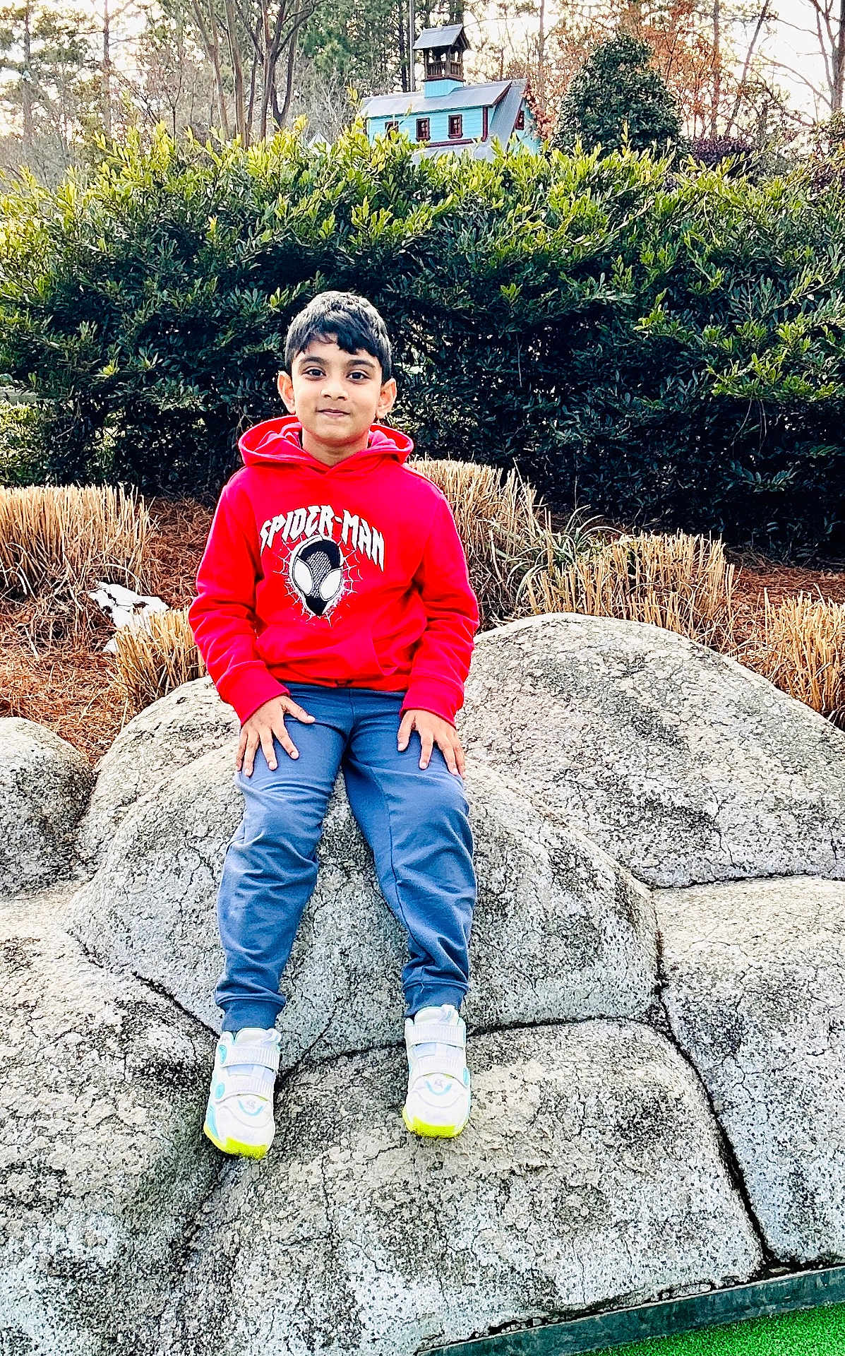 Aayan joined the competition — help win amazing prizes! child, boy, red_hoodie, spiderman, blue_pants, sneakers, rock, outdoor, nature, greenery, bushes, model_house, casual_clothing, portrait, sitting, daylight, young, smiling, park, relaxed
