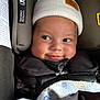 baby, child, car_seat, hat, white_hat, blanket, smile, face, infant, closeup, cute, warm_clothing, straps, safety, indoors, expression, cheeky, young_child, cozy, seat