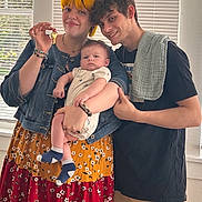 August is registered to the contest to win money with this photo: family, woman, man, baby, indoor, window, blinds, key, smile, holding, casual_clothing, bracelet, dress, denim_jacket, short_hair, facial_expression, portrait, toddler, happy, people