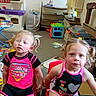 Emily And Allison joined the competition — help win amazing prizes! children, girls, toddlers, siblings, portrait, sitting, chairs, playroom, toys, toy_kitchen, books, clutter, indoor, home, blonde_hair, pigtails, smiling, casual_clothing, colorful, photograph