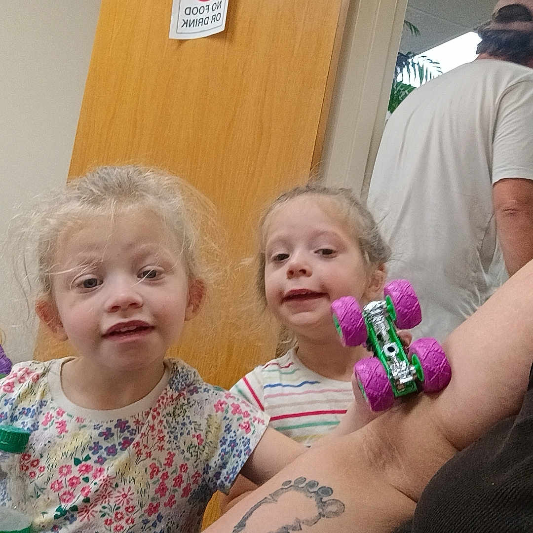 Emily And Allison joined the competition — help win amazing prizes! children, girls, twins, toddler, smiling, portrait, indoor, door, wooden_door, adult, arm, tattoo, toy, colorful_toy, wheels, floral_dress, striped_shirt, blonde_hair, no_food_sign, family