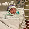 newborn, baby, sleeping, hospital, bassinet, swaddled, knit_cap, pacifier, medical_monitor, blanket, crib, infant, portrait, indoors, peaceful, resting, face, head, healthcare, photography
