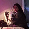 person, puppy, dog, white_dog, black_markings, pet, hugging, portrait, indoor, dim_lighting, pink_lighting, chair, table, plate, window, long_hair, face, sitting, home, candid