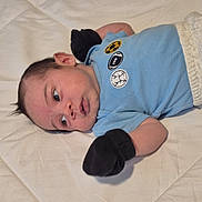 Erick Martín joined the competition — help win amazing prizes! baby, infant, lying_down, blue_shirt, black_mittens, quilted_bedspread, curious, face, head, clothing, cute, child, one_person, indoor, young_child, skin, portrait, baby_garment, expression, hair