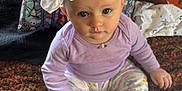 Eden is registered to the contest to win money with this photo: baby, bow, carpet, child, closeup, curious, cute, face, floral_pants, headband, home, indoor, infant, pattern, person, pillow, purple_shirt, sitting, sock, soft_lighting