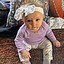 baby, bow, carpet, child, closeup, curious, cute, face, floral_pants, headband, home, indoor, infant, pattern, person, pillow, purple_shirt, sitting, sock, soft_lighting