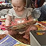 basket, book, carpet, child, clothing, colorful, curiosity, floor, foot, furniture, hand, home, indoor, person, pigtails, play, portrait, reading, toddler, toys