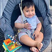Nikolai is registered to the contest to win money with this photo: baby, child, smiling, baby_rocker, bib, striped_onesie, soft_book, toy, feet, happy, seatbelt, baby_seat, outdoor, daylight, fabric, mesh_back, plastic, playful, cute, infant