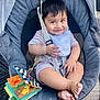 baby, child, smiling, baby_rocker, bib, striped_onesie, soft_book, toy, feet, happy, seatbelt, baby_seat, outdoor, daylight, fabric, mesh_back, plastic, playful, cute, infant