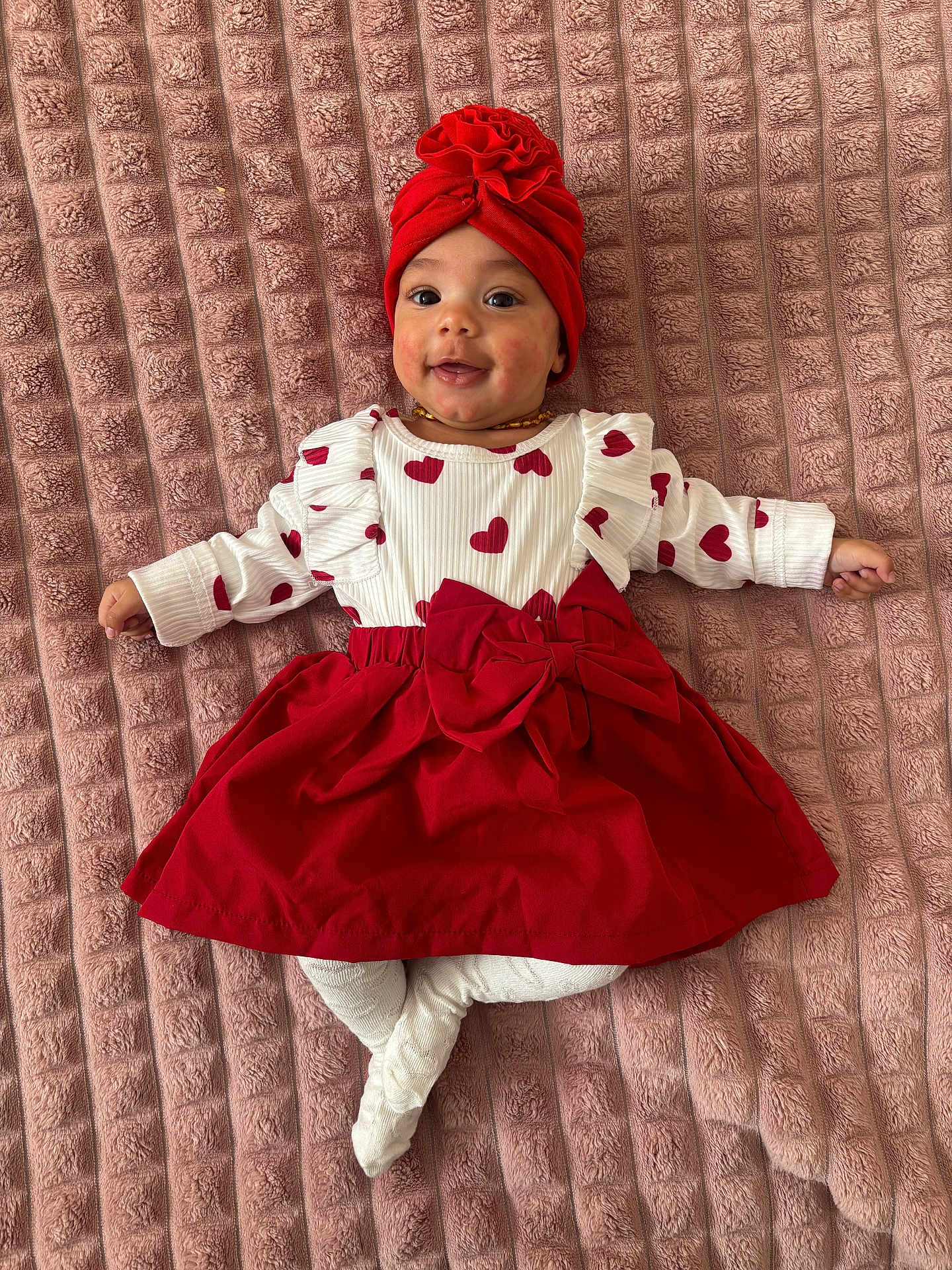 Inaya participe au concours pour gagner de l'argent avec cette photo : baby, infant, smiling, red_turban, red_dress, white_tights, heart_pattern, blanket, lying_down, cute, happy, child, portrait, indoor, fashion, headwear, one_person, young_child, soft_texture, baby_clothes