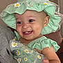 baby, child, smiling, hat, dress, daisies, green_clothing, person, indoor, happy, cute, face, hand, infant, headwear, apparel, holding, closeup, portrait, human