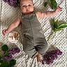 baby, infant, romper, blanket, purple_flowers, green_leaves, milestone_card, face, drool, cute, lying_down, soft_texture, indoor, child, person, adorable, young, portrait, month_marker, nature_elements