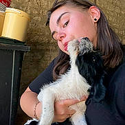 Athéna a rejoint le concours — aidez-le/la à gagner de superbes lots ! woman, dog, pet, licking, affection, holding, black_and_white, cute, indoor, portrait, casual, stone_wall, bracelet, earring, glasses, short_hair, closeup, love, animal, human