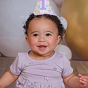 Harper is registered to the contest to win money with this photo: baby, child, smiling, party_hat, birthday, one_year_old, curly_hair, purple_dress, indoor, balloons, celebration, happy, cute, portrait, person, infant, sitting, floor, festive, young