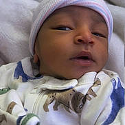 Masai is registered to the contest to win money with this photo: baby, newborn, infant, onesie, hat, beanie, animal_print, blanket, sleepy, face, cute, cozy, clothing, person, portrait, indoor, soft, water_bottle, lying_down, newborn_clothing