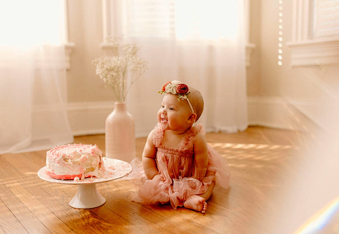 Lola is registered to the contest to win money with this photo: child, dessert, doll, floor, flooring, hardwood, headpiece, icing, peach, person, pink, porcelain, room, serveware, sitting, sweetness, tableware, teddy_bear, toy, window