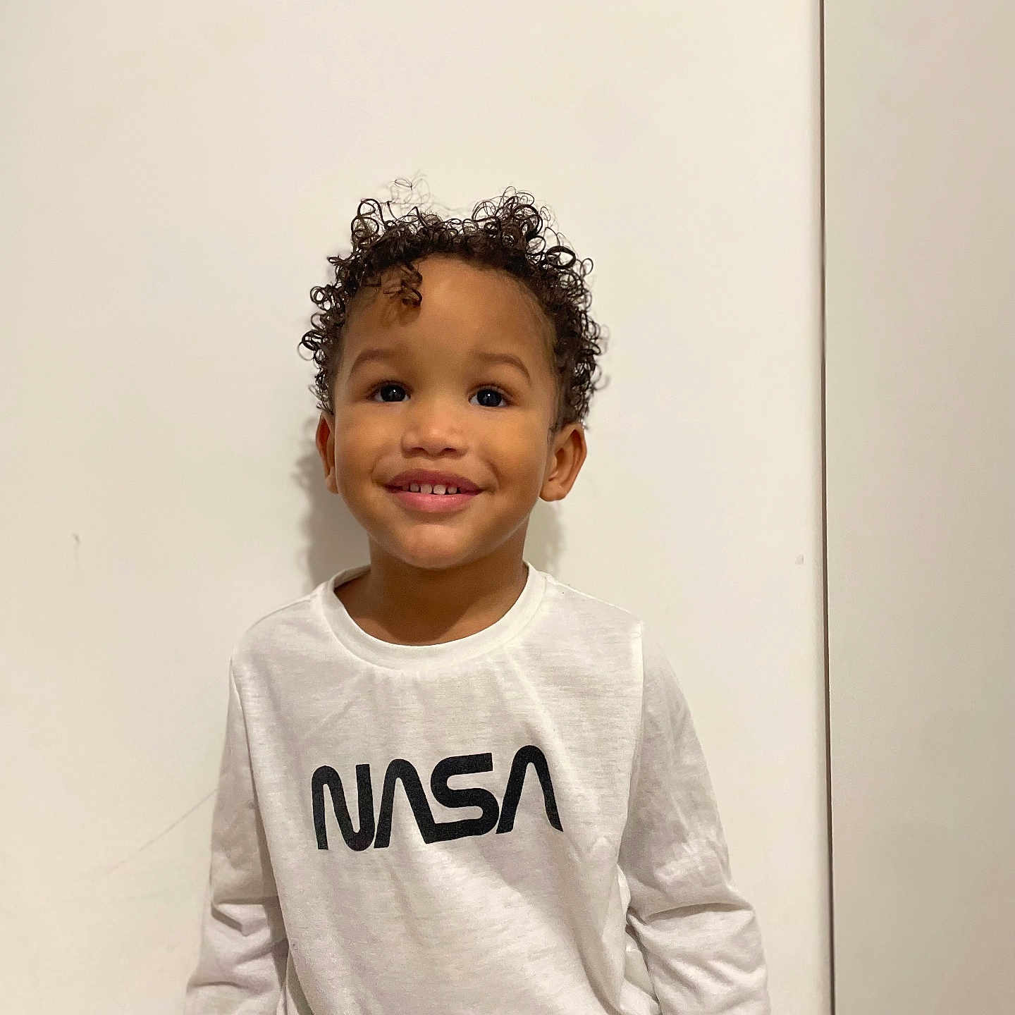 Tidiane a rejoint le concours — aidez-le/la à gagner de superbes lots ! casual_clothing, child, curly_hair, cute, eyes, hair, happy, indoors, minimalist, nasa_logo, portrait, skin, smiling, standing, studio, teeth, tshirt, vertical_photo, white_wall, young_child