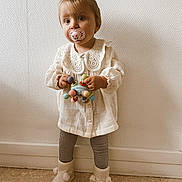 Thaïs a rejoint le concours — aidez-le/la à gagner de superbes lots ! toddler, child, pacifier, toy, white_blouse, lace_collar, pigtails, hair_bows, boots, checkered_leggings, standing, indoors, textured_wall, floor, cute, young_child, portrait, innocence, clothing, person