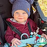 Liam joined the competition — help win amazing prizes! toddler, child, hat, knit_hat, pom_poms, stroller, blanket, smile, happy, outdoor, clothing, seatbelt, baby_toy, person, portrait, cute, warm_clothing, daylight, face, infant