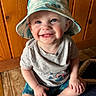 Liam is registered to the contest to win money with this photo: baby, blue_eyes, bucket_hat, casual_clothing, child, cute, floor, happy, hat, indoor, person, portrait, rug, shorts, sitting, smiling, toddler, tshirt, wooden_wall, young_child