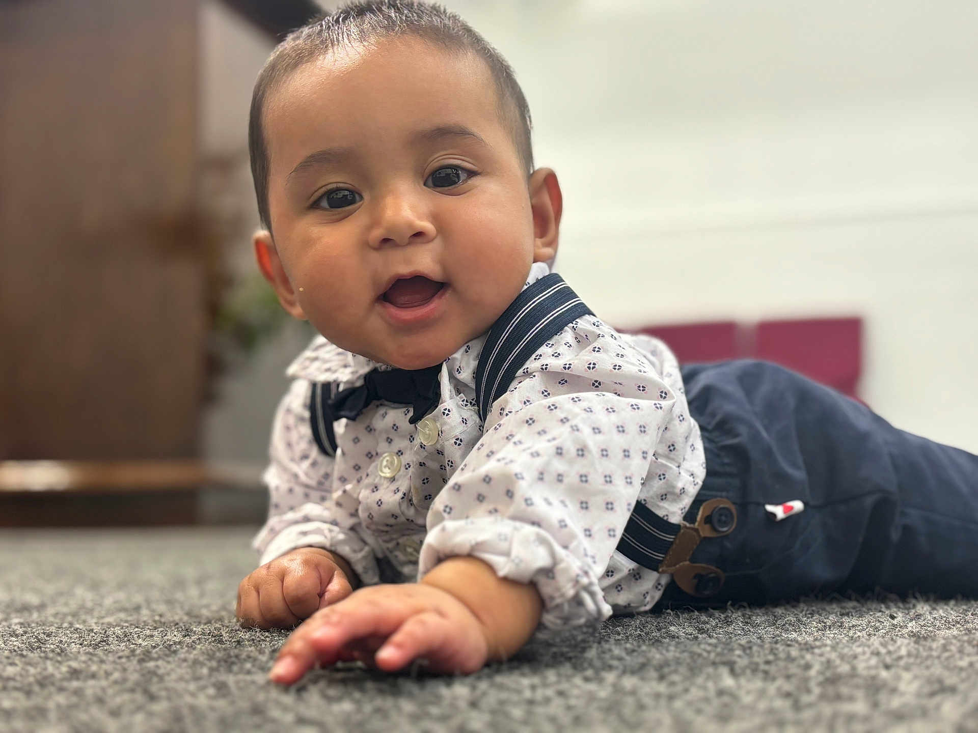 Natanael is registered to the contest to win money with this photo: baby, child, crawling, carpet, face, hands, clothing, shirt, suspenders, bow_tie, indoors, portrait, cute, happy, smiling, infant, person, young_child, focus, background_blur
