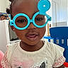 Erza is registered to the contest to win money with this photo: toddler, child, glasses, toy, blue_glasses, white_shirt, sparkly_cat, pink_bow, indoor, playroom, furniture, smile, face, portrait, cute, happy, person, hair, earrings, young_child