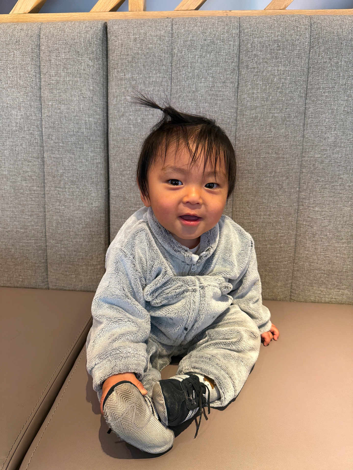 Noah participe au concours pour gagner de l'argent avec cette photo : toddler, child, baby, smiling, sitting, onesie, fuzzy_clothing, shoe, shoe_sole, hair_tuft, bench, cushion, gray_background, indoor, cute, happy, person, face, cozy, playful