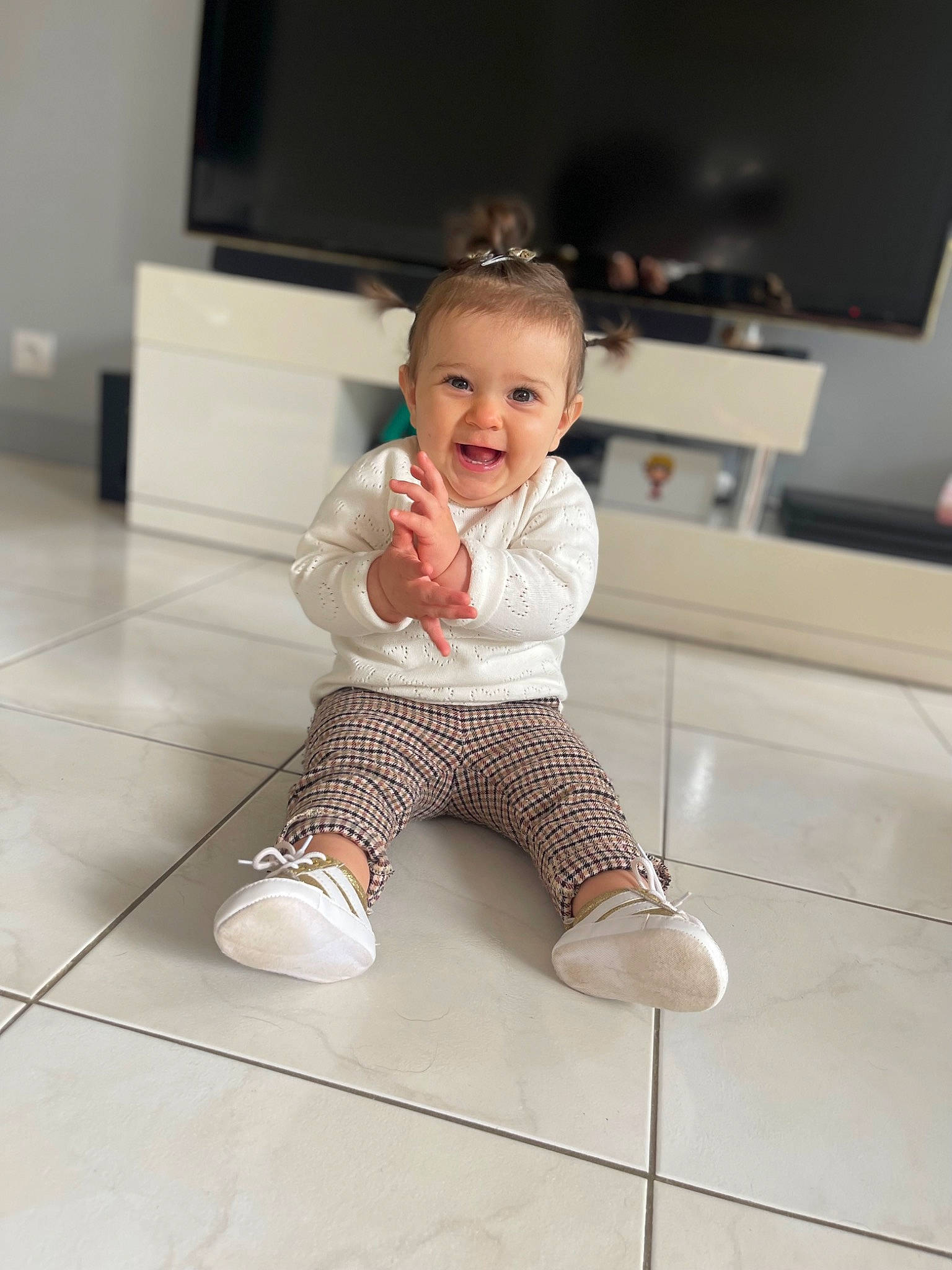 Aïnara participe au concours pour gagner de l'argent avec cette photo : baby, baby_toddler_clothing, cheek, child, comfort, face, floor, flooring, happy, hardwood, head, home_appliance, human_leg, knee, person, sleeve, smile, t_shirt, television, toddler