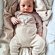 Gabriella a rejoint le concours — aidez-le/la à gagner de superbes lots ! baby, infant, child, blanket, knit_pants, hat, cozy, soft, cute, portrait, lying_down, beige, warm_colors, newborn, clothing, sleepwear, toddler, face, hand, foot