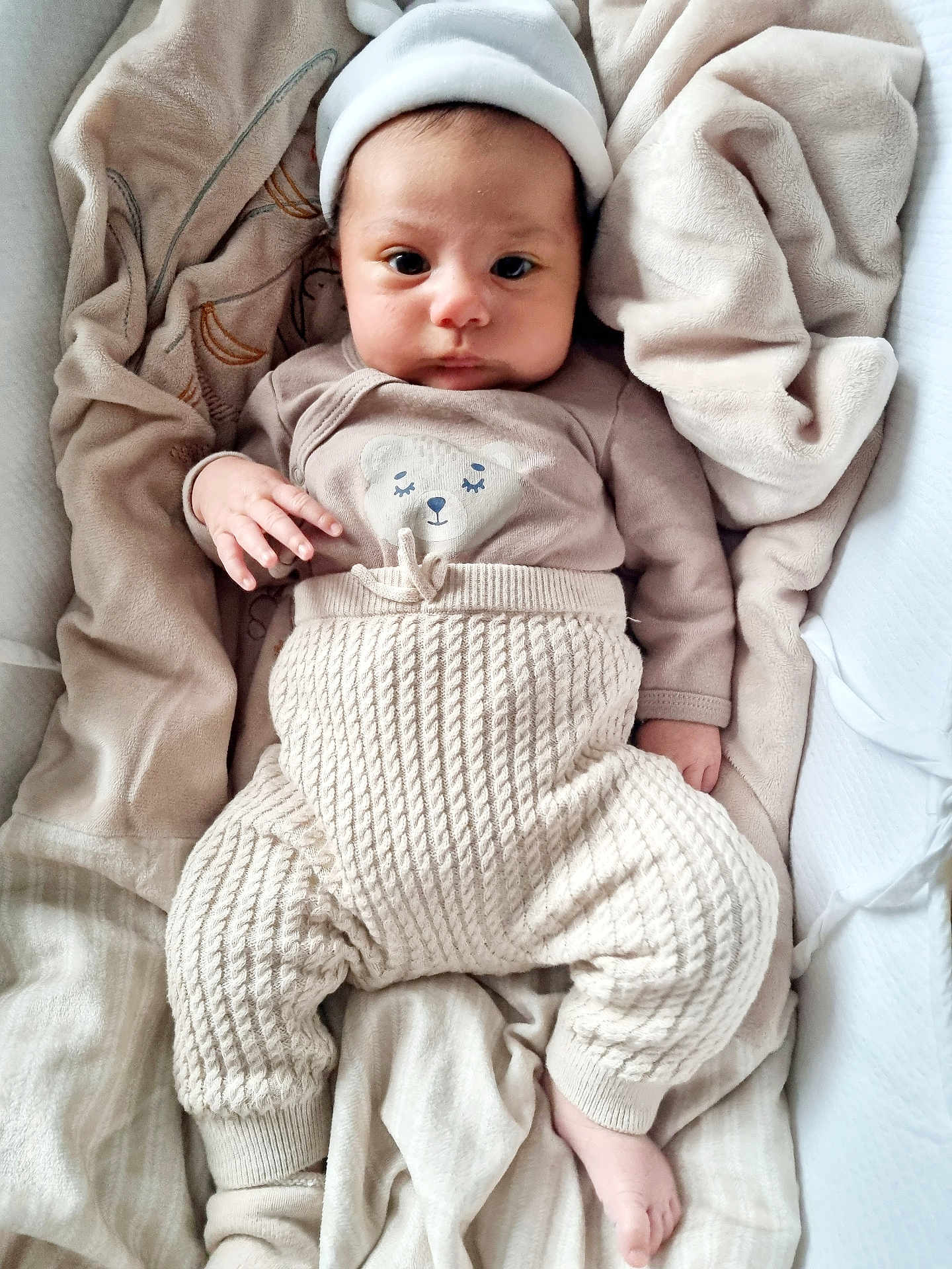 Gabriella a rejoint le concours — aidez-le/la à gagner de superbes lots ! baby, infant, child, blanket, knit_pants, hat, cozy, soft, cute, portrait, lying_down, beige, warm_colors, newborn, clothing, sleepwear, toddler, face, hand, foot