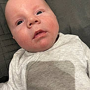 Nicolas joined the competition — help win amazing prizes! baby, infant, face, skin, onesie, clothing, lying_down, expression, eyes, head, human, child, portrait, closeup, indoors, shadow, fabric, texture, light, skin_detail