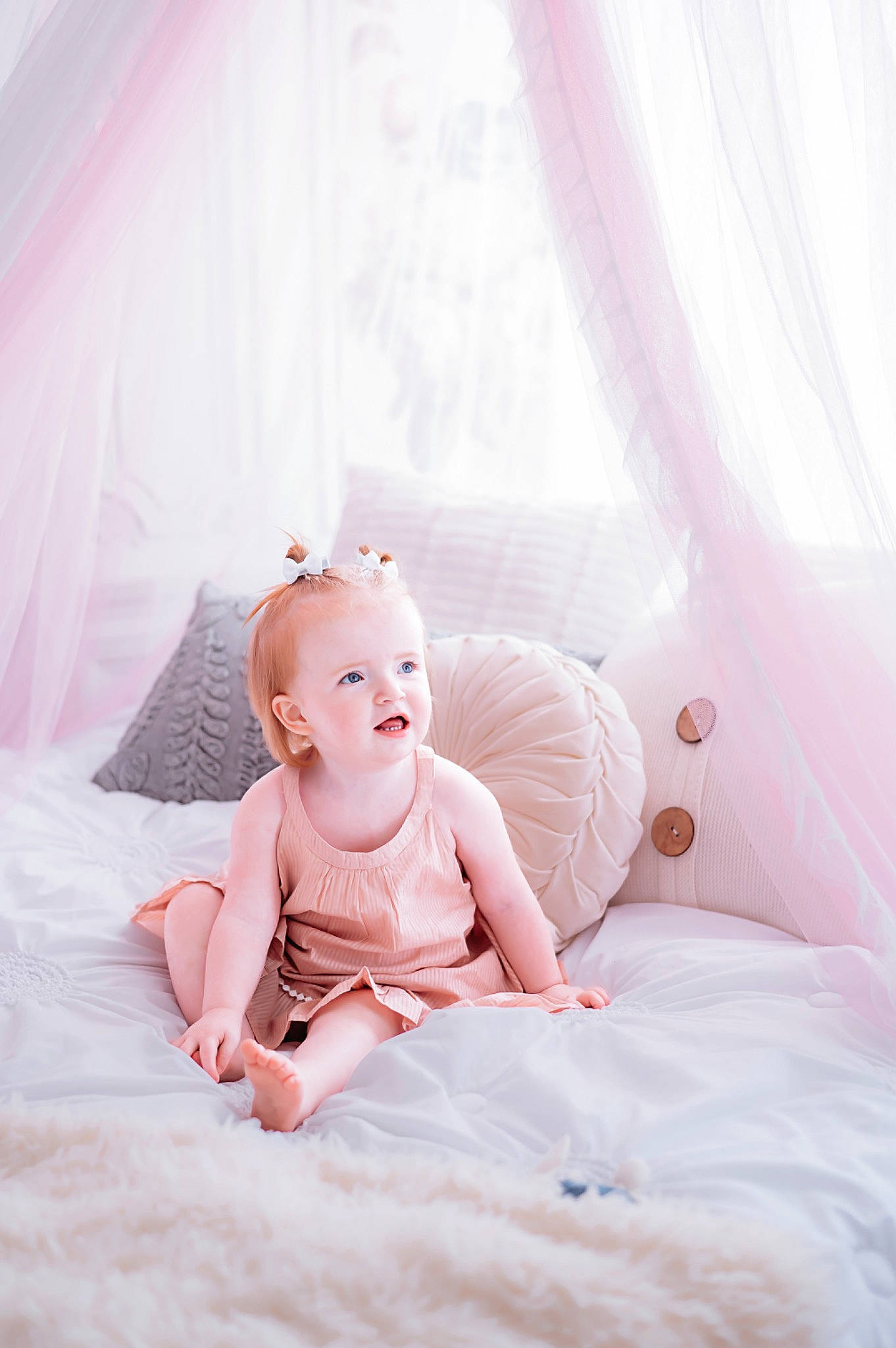 Emersyn is registered to the contest to win money with this photo: arm, baby, baby_toddler_clothing, bed, bedding, comfort, curtain, dress, flash_photography, flooring, hand, happy, human_body, linens, magenta, peach, person, pink, sitting, smile