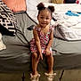 child, girl, bed, pillow, blanket, slippers, animal_slippers, dress, indoor, floor, smile, hair, pigtails, furniture, room, toy, footwear, person, cute, cozy