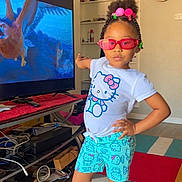 Journey is registered to the contest to win money with this photo: child, girl, standing, pose, indoor, living_room, television, animation, hello_kitty, tshirt, shorts, sneakers, sunglasses, colorful, hair_beads, carpet, furniture, clock, cable, casual_clothing