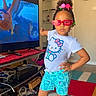 child, girl, standing, pose, indoor, living_room, television, animation, hello_kitty, tshirt, shorts, sneakers, sunglasses, colorful, hair_beads, carpet, furniture, clock, cable, casual_clothing