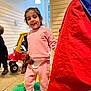 child, smiling, pink_clothing, teddy_bear, indoor, playroom, toy_car, boots, happy, person, floor, light, window, wall, play, fun, cute, young_child, standing, daylight