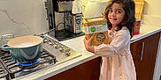 Aadya is registered to the contest to win money with this photo: child, girl, kitchen, pasta_box, stove, cooking, pot, step_stool, socks, dress, smile, cabinet, countertop, appliance, boiling_water, wooden_floor, coffee_machine, happy, indoor, curly_hair