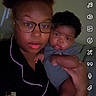 Tyaire is registered to the contest to win money with this photo: person, baby, glasses, indoor, selfie, holding, face, child, dark_background, clothing, technology, social_media_interface, portrait, human, parent, infant, casual, expression, hand, screen