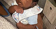 Tyaire joined the competition — help win amazing prizes! baby, infant, child, bib, clothing, person, hand, face, curly_hair, indoor, blanket, furniture, drawer, socks, holding, looking, expression, skin, cute, newborn