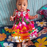 Djéliya a rejoint le concours — aidez-le/la à gagner de superbes lots ! baby, bright_colors, child, clothing, colorful, couch, curious, cute, dress, fabric, floral_pattern, happy, indoors, infant, patterned, person, portrait, sitting, small_toes, toddler