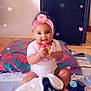 baby, infant, child, toy, blanket, headband, pink, heart_effects, floor, indoor, smiling, cute, sitting, colorful, playful, happy, person, clothing, appliance, floor_tiles