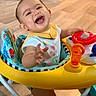 baby, baby_toy, child, clothing, colorful, expression, face, flooring, hand, happy, indoor, infant, joy, person, play, reaching, seat, smiling, toy, walker