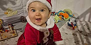 Emy participe au concours pour gagner de l'argent avec cette photo : baby, bed, blanket, child, christmas_outfit, cute, festive, happy, holiday, indoor, infant, person, playful, plush, red_clothing, santa_hat, smiling, striped_socks, toys, white_fur_trim