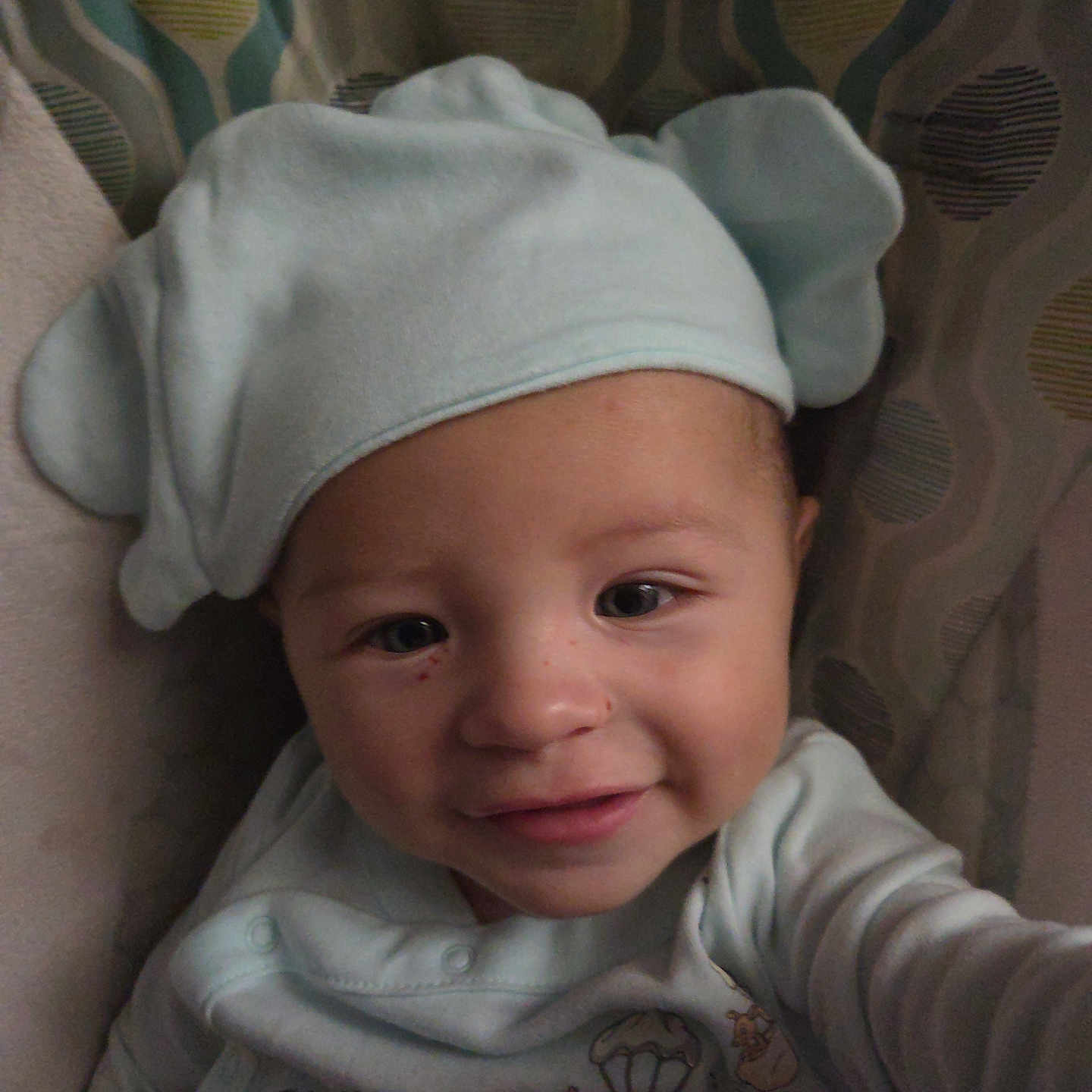 Liam joined the competition — help win amazing prizes! baby, baby_garment, child, childrens_clothing, closeup, clothing, cute, face, happy, hat, headwear, indoors, infant, patterned_background, person, portrait, smiling, soft_toy, warm, young_child