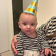 Darya a rejoint le concours — aidez-le/la à gagner de superbes lots ! baby, celebration, child, closeup, curious_expression, cute, door, dress, face, floor_tiles, hand, holding, indoor, long_hair, party_hat, patterned_clothing, person, striped_clothing, striped_shirt, white_wall