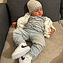 Menzo a rejoint le concours — aidez-le/la à gagner de superbes lots ! toddler, child, couch, jeans, striped_shirt, white_sneakers, beanie, jacket, indoor, soft_furniture, relaxed, casual_clothing, footwear, sitting, young_child, light_blue_jeans, patterned_hat, comfortable, home, portrait