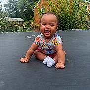 Legend joined the competition — help win amazing prizes! baby, child, smiling, sitting, outdoor, trampoline, grass, house, brick, greenery, shirt, socks, happy, playful, nature, daylight, portrait, cute, infant, person