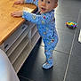 Lyam participe au concours pour gagner de l'argent avec cette photo : blue, blue_eyes, books, child, couch, curious, face, floor, holding, indoor, living_room, pajamas, person, pillow, standing, table, tiles, toddler, toy, wooden_table