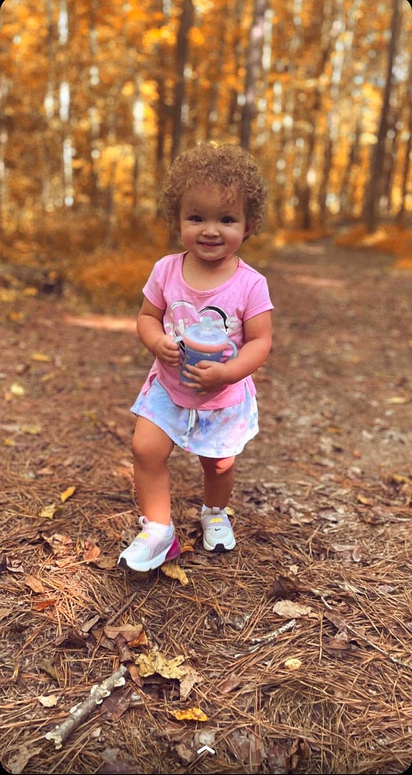 Sage is registered to the contest to win money with this photo: adaptation, branch, forest, grass, happy, joy, leisure, mammal, morning, natural_environment, people_in_nature, person, plant, shorts, smile, standing, sunlight, t_shirt, toddler, tree